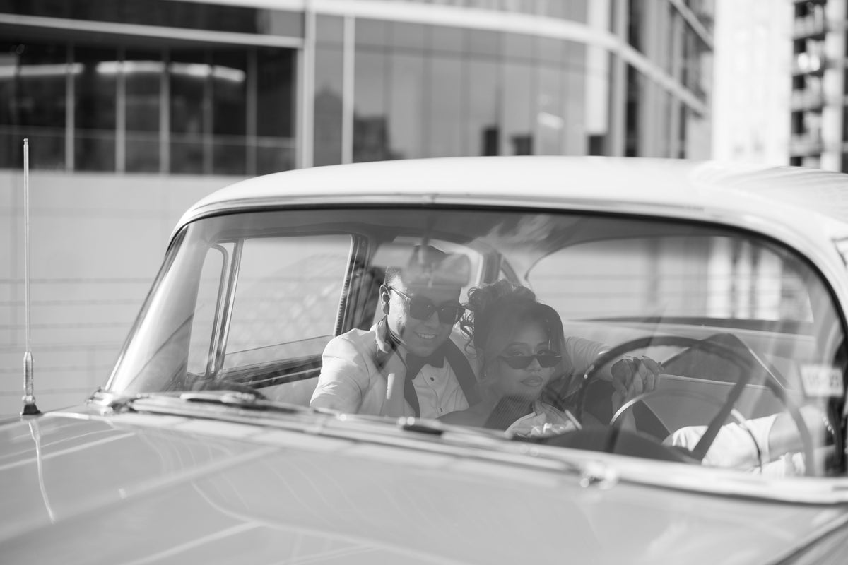 Black-and-white portrait of a couple photographed through the windshield of a Chevrolet Bel Air in Houston 