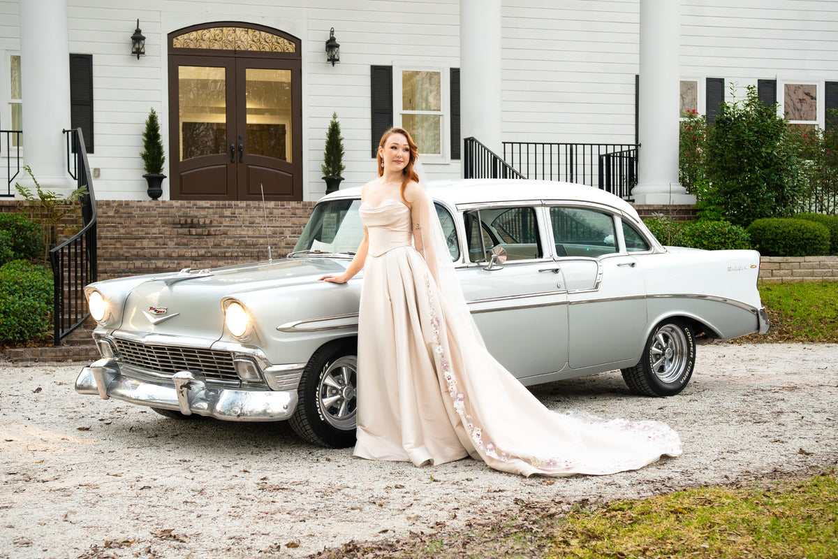 Bride in a wedding gown posing beside a white 1956 Chevrolet Bel Air at a Houston wedding venue