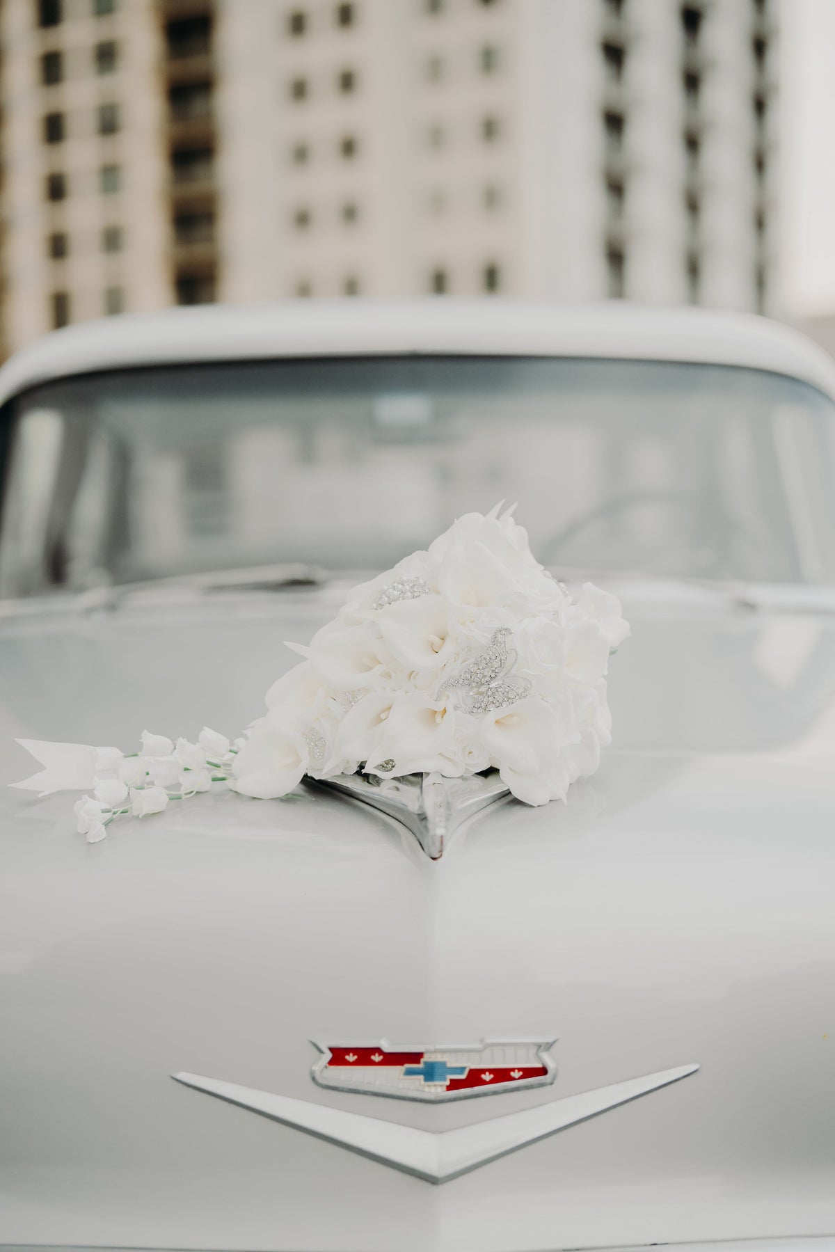 White wedding bouquet resting on the hood of a 1956 Chevrolet Bel Air